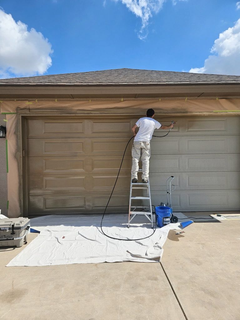 A painter on a ladder working on a garage door